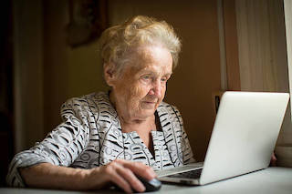 Anziana signora che siede al tavolo ed usa il suo computer